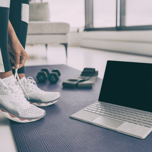 Sportschuhe, Hantel und ein Terraband neben einem Laptop